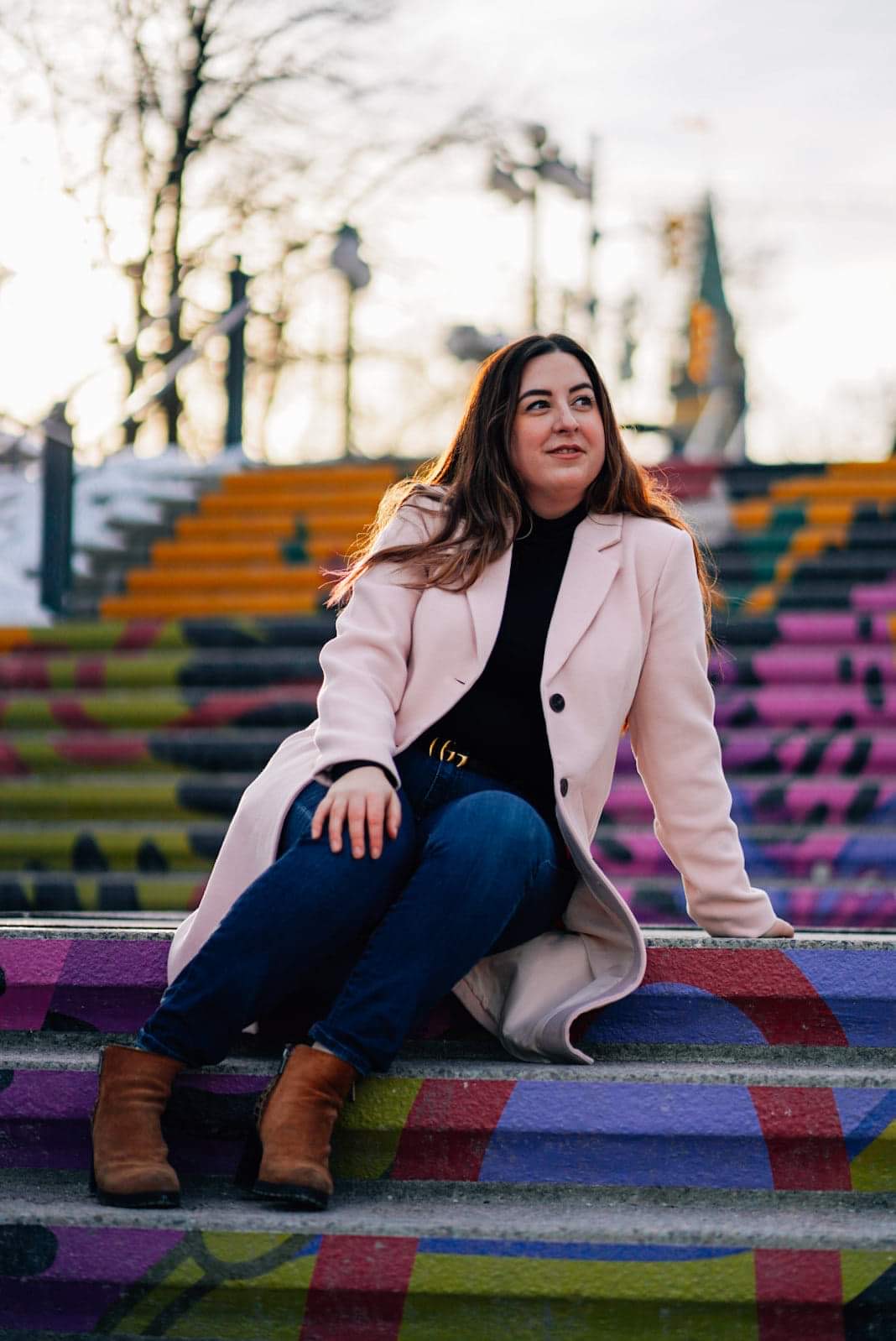 Georgia is sitting on an outdoor painted staircase in a pink coat